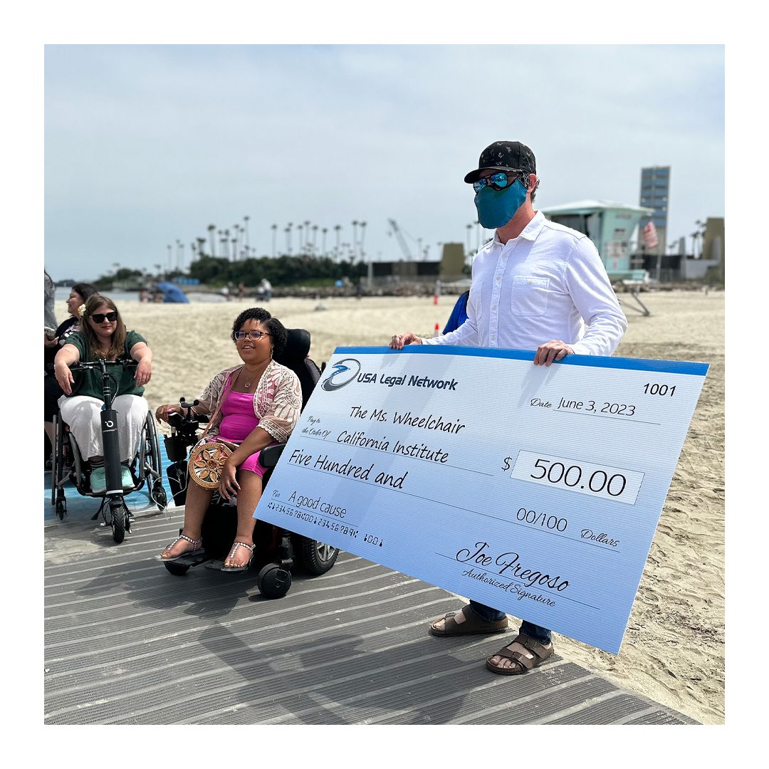 Picture of Joe at the beach with a big check for The Ms. Wheelchair California Institute for five hundred dollars